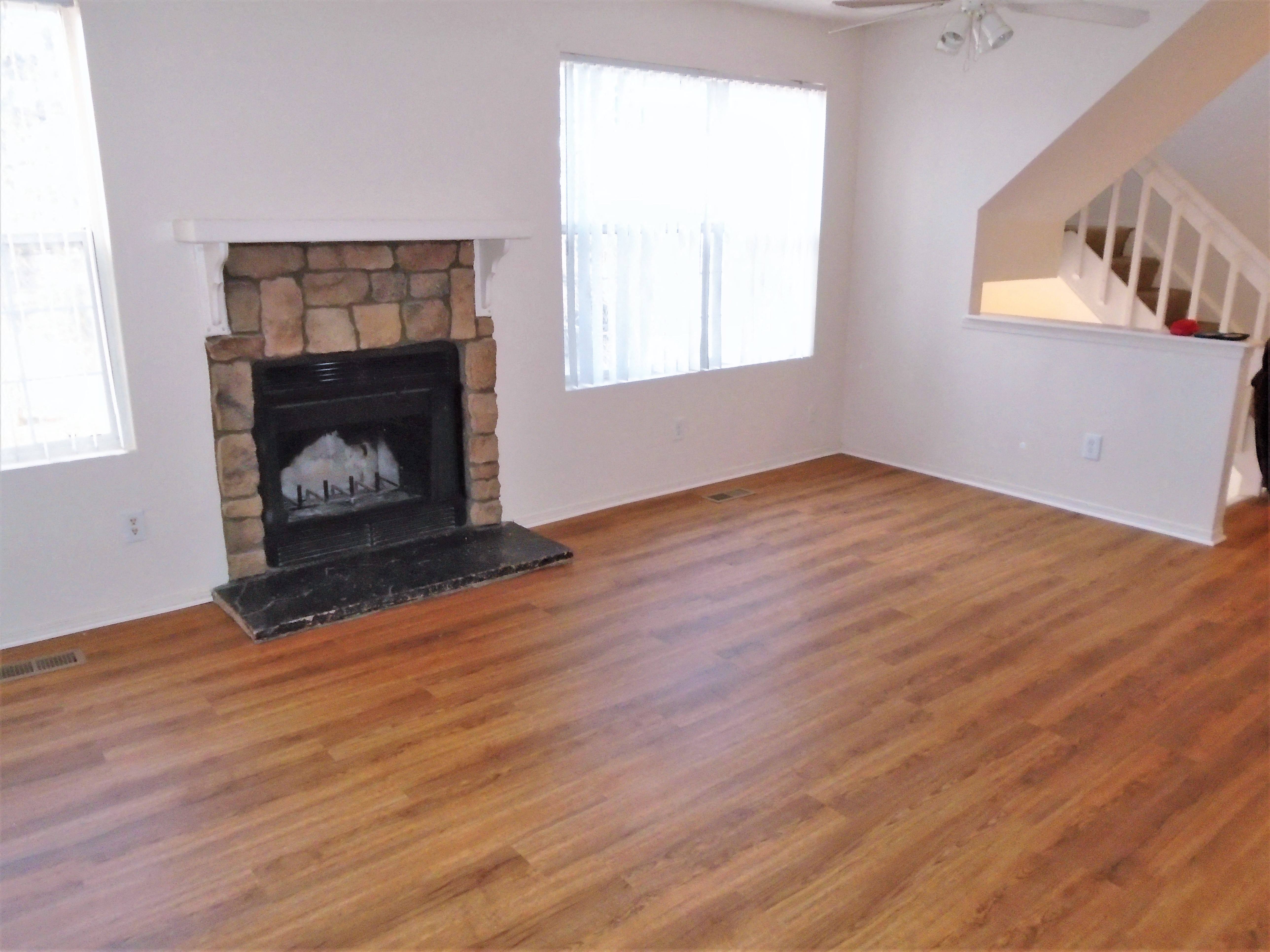A living room with wood style flooring, white walls, windows, and fireplace